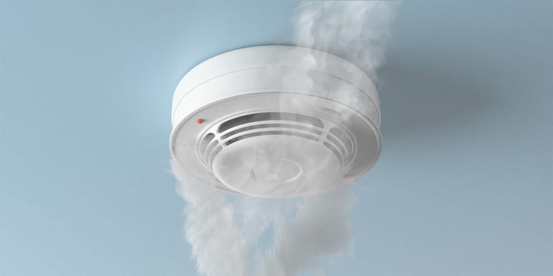 Une photo en gros plan d'un détecteur de fumée monté au plafond avec de la fumée blanche et un voyant rouge